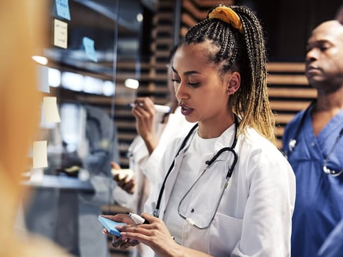 Adult female nurse taking notes while collaborating with other clinicians