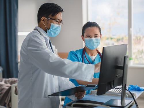 Doctor and nurse wearing masks working together on a computer on wheels (COW)