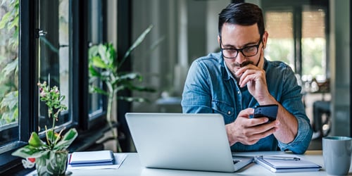 Adult man working at his desk using his smart phone and laptop