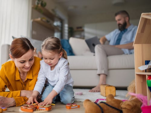 Adult male doctor working from home using his laptop while his wife and daughter play on the floor