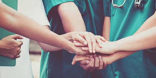 Clinicians in green and white scrubs with hands on top of each other