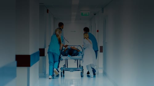 Team of doctors and nurses pushing a patient in a gernie running down a hospital emergency room hallway