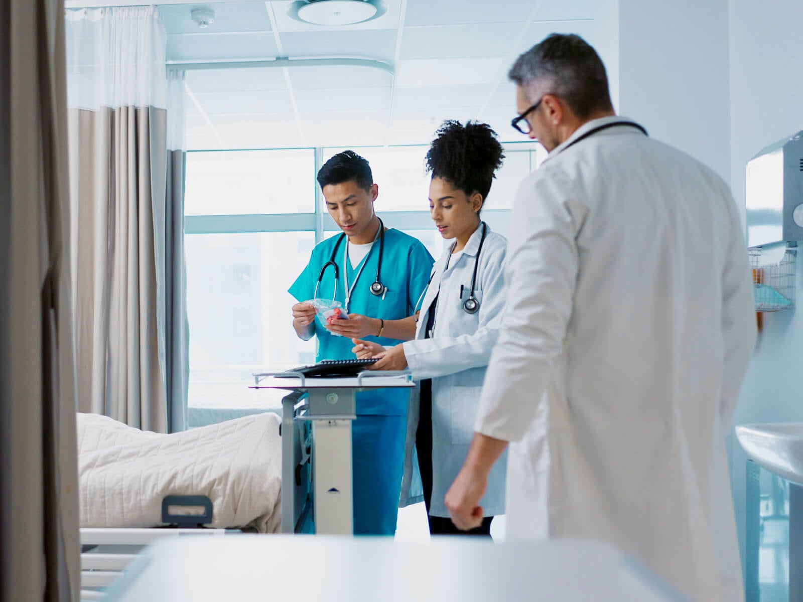 A care team of two nurses and a physician reviewing patient information at a bedside workstation in an acute care hospital room